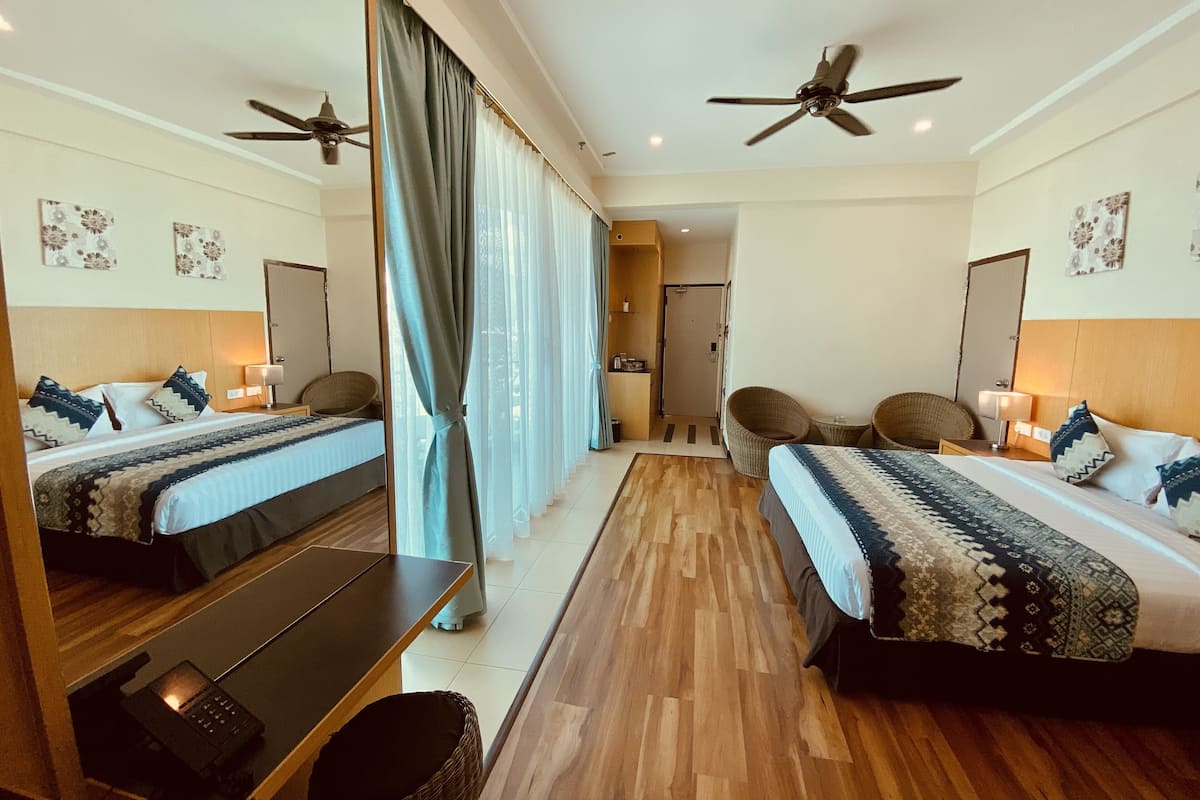 A hotel room with two beds, a desk, a chair, a ceiling fan, and a mirror.