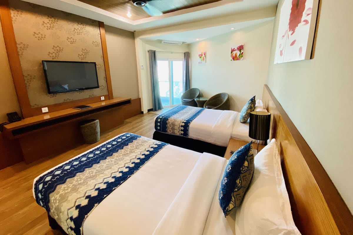A hotel room with two beds, a TV mounted on the wall, a ceiling fan, and a view of the outdoors.