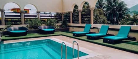A swimming pool with lounge chairs and a small hot tub.