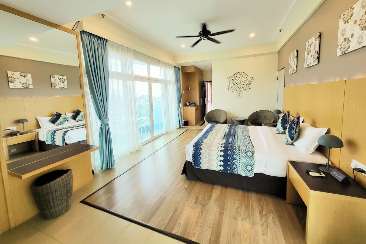 A modern hotel room with a large bed, a sitting area with two chairs, a small table, and a ceiling fan.
