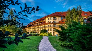 A hotel with a curved roof, multiple balconies, and a paved pathway leading to the entrance. - Hotel Ossa Conference & Spa (Rawa Mazowiecka)