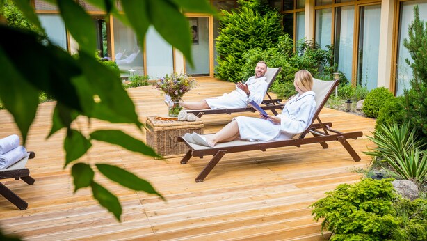 A wooden deck with two lounge chairs, a wicker basket, and a small table with a vase of flowers. - Hotel Ossa Conference & Spa (Rawa Mazowiecka)