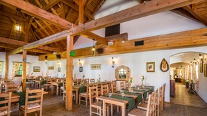 A rustic dining hall with wooden tables and chairs, high ceilings with exposed beams, and wall-mounted lighting fixtures. - Hotel Ossa Conference & Spa (Rawa Mazowiecka)