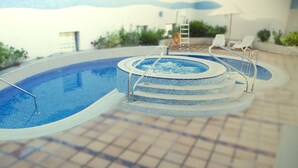 A swimming pool with a hot tub, surrounded by lounge chairs and a tiled deck. - Grand Belle Vue (Dubai)