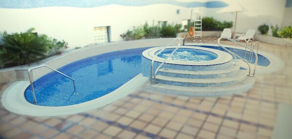 A swimming pool with a hot tub, surrounded by lounge chairs and a tiled deck.