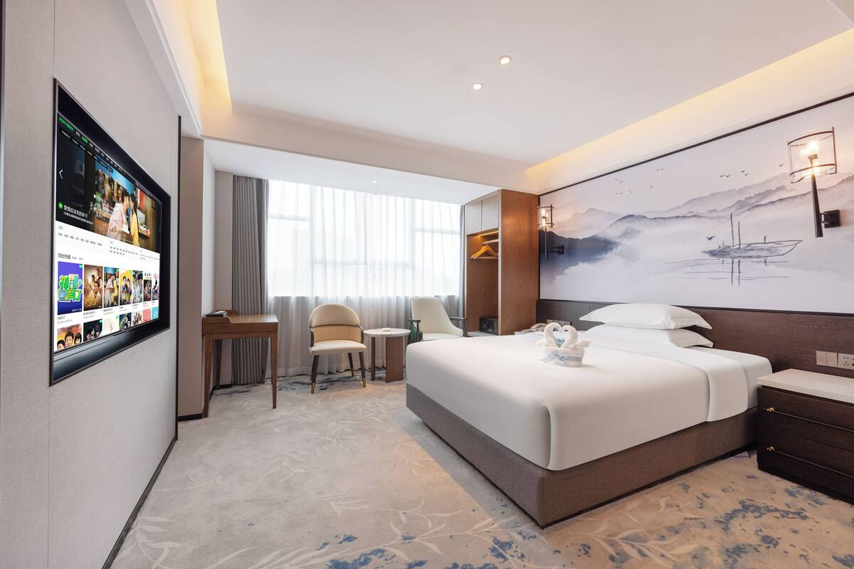 Une chambre d’hôtel avec un grand lit, un bureau, une chaise, un téléviseur fixé au mur et un tableau accroché au mur.