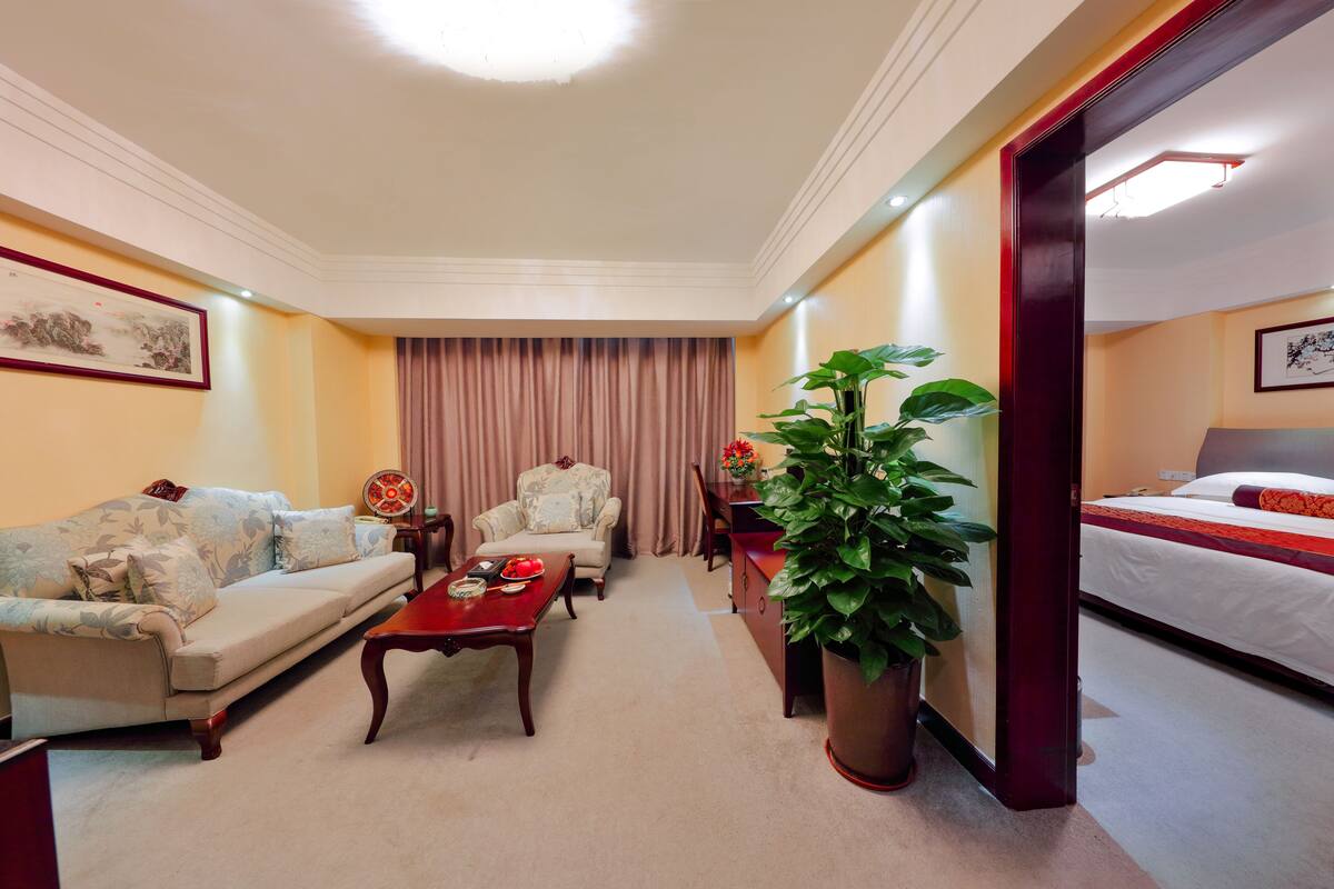 Une chambre d’hôtel avec un canapé, un fauteuil, une table basse, une plante en pot et un lit.
