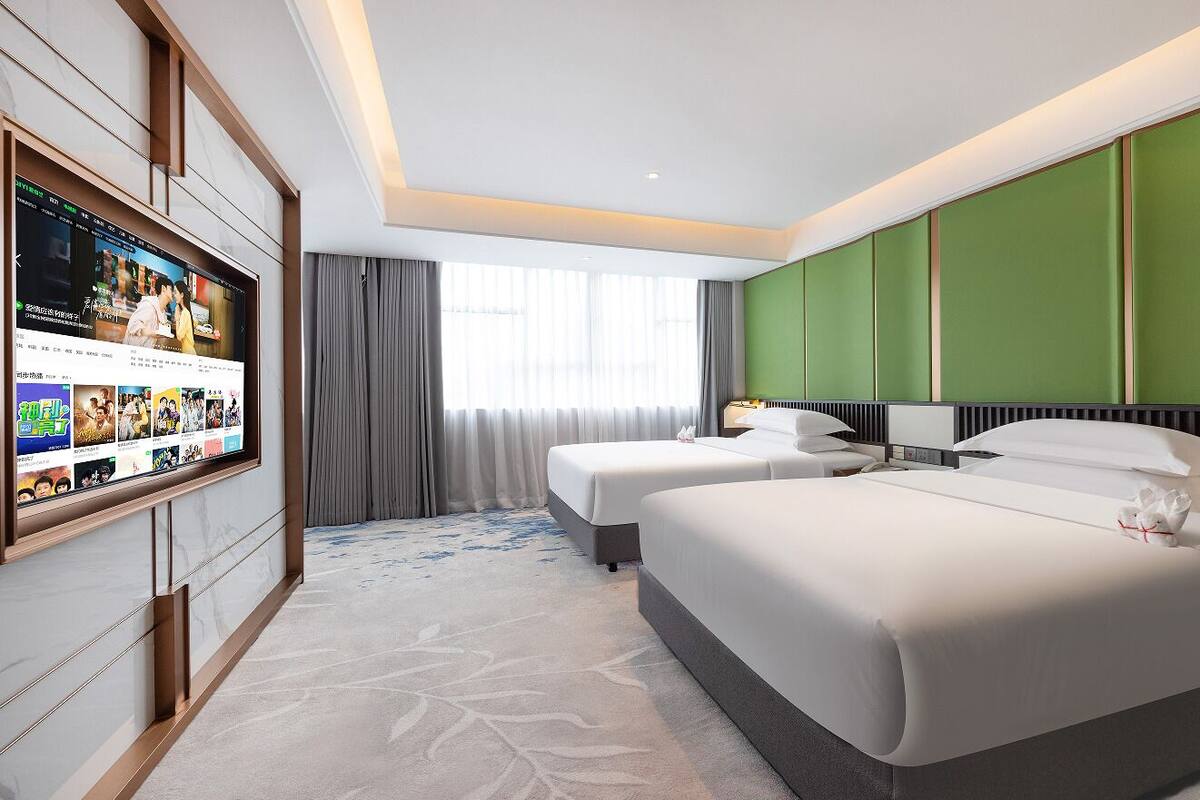 Une chambre d’hôtel avec deux lits, un grand téléviseur à écran plat fixé au mur et une fenêtre avec des rideaux.