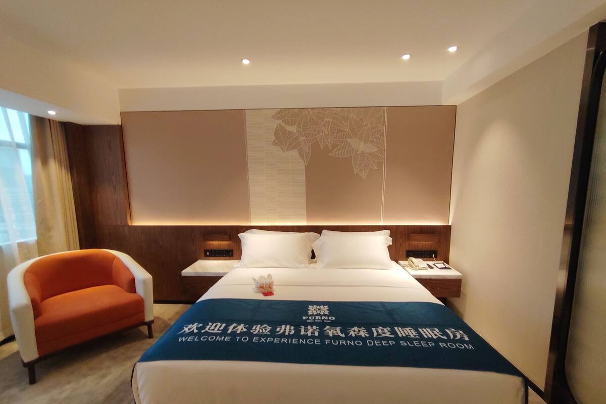 Une chambre d’hôtel avec un lit, une table de chevet, une chaise et une grande fenêtre.