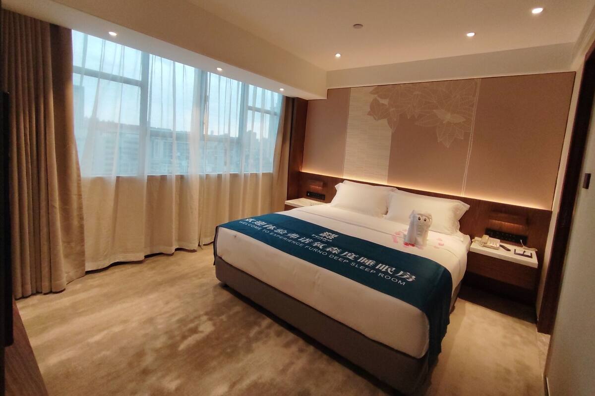 Une chambre d’hôtel avec un grand lit, une table de chevet avec un téléphone et une fenêtre avec des rideaux.