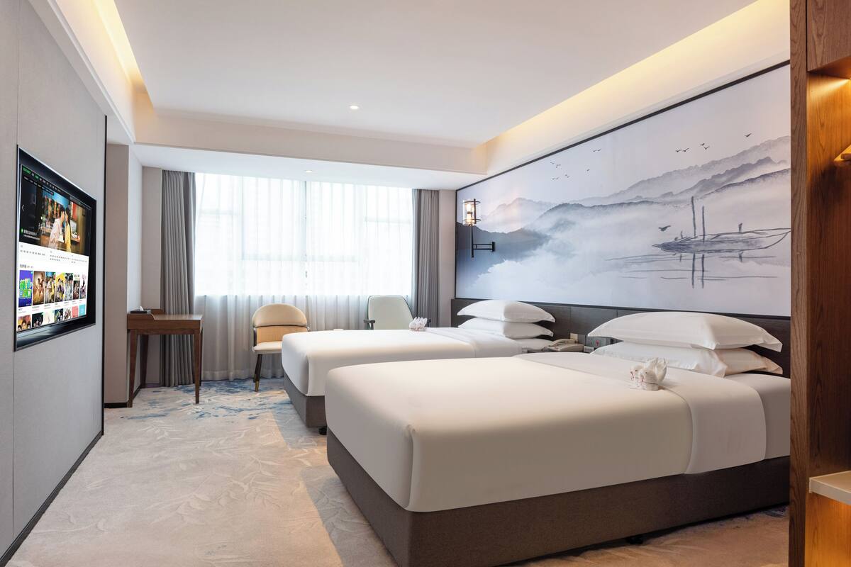 Une chambre d’hôtel avec deux lits, un bureau, une chaise, une télévision et un grand tableau au mur.