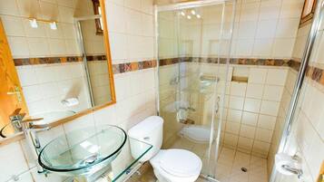 A bathroom with a glass sink, white toilet, and a glass-enclosed shower.