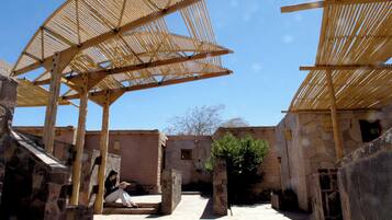 A courtyard with stone buildings, wooden pergolas, and a person sitting on a bench.