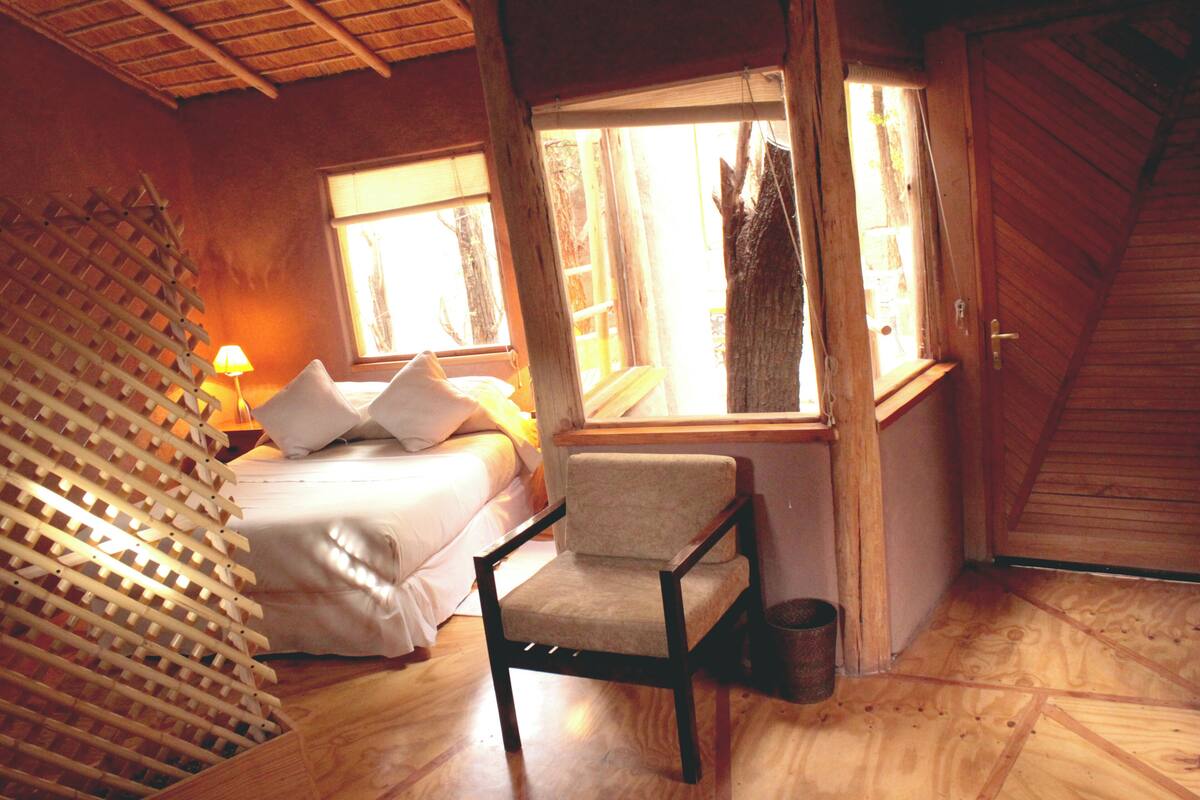 A cozy room with a bed, a chair, a window, and a wooden ceiling.
