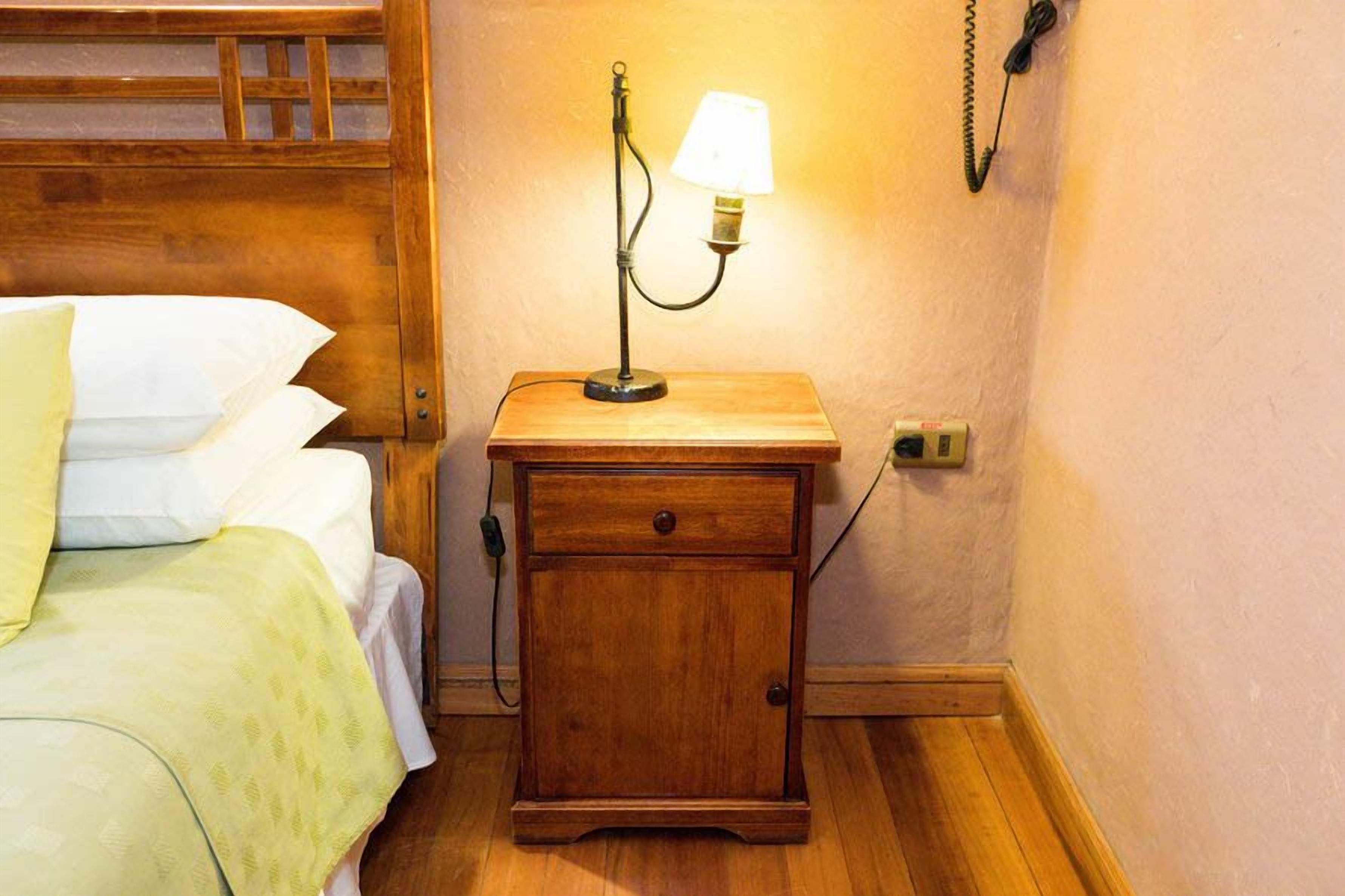 A wooden bedside table with a lamp, a drawer, and a telephone.