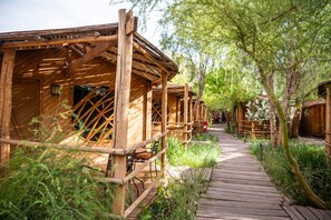 A wooden pathway leading to rustic wooden cabins surrounded by greenery. - Hotel Kimal (San Pedro de Atacama)