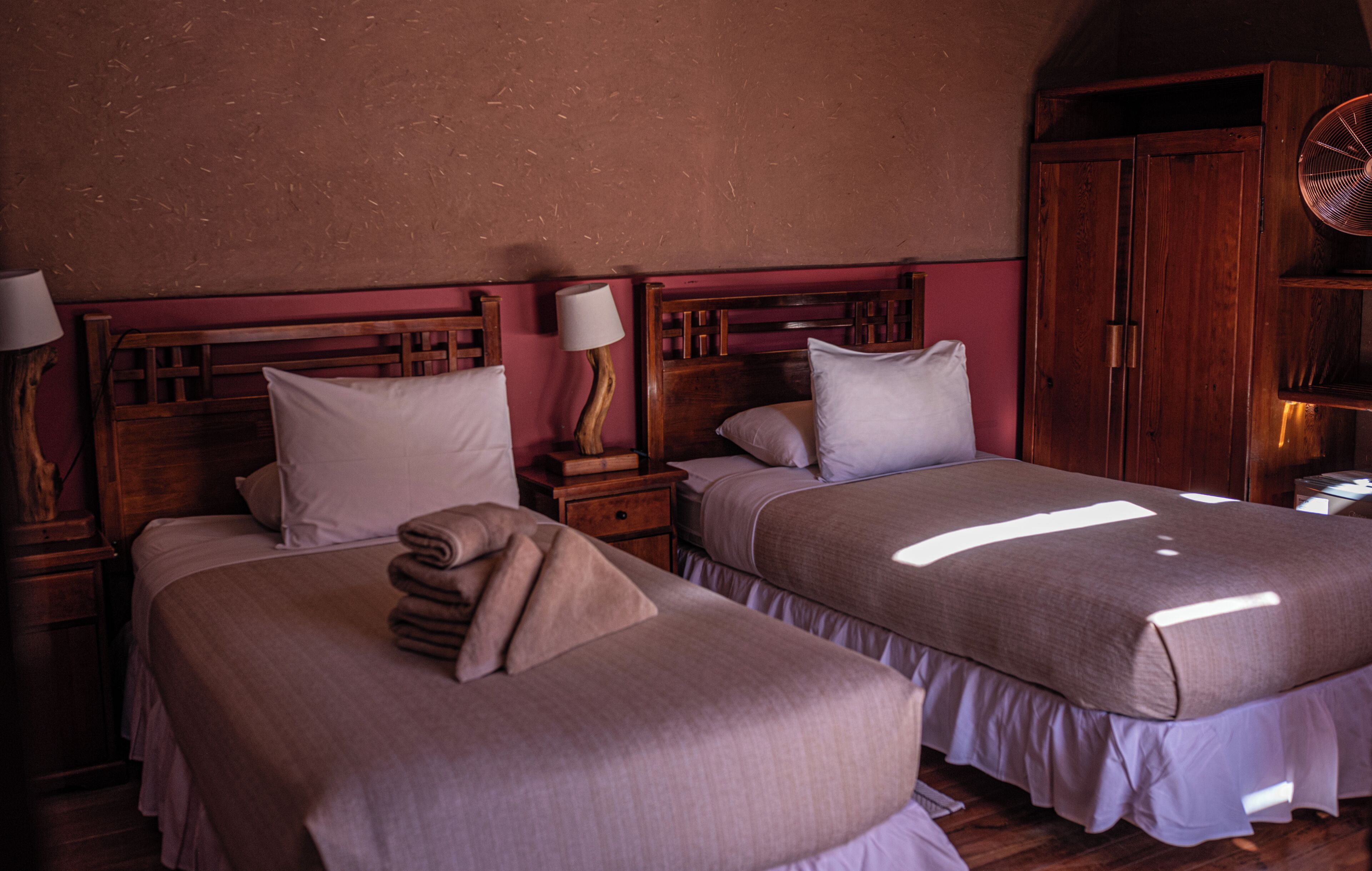 Een kamer met twee bedden, houten hoofdborden, een nachtkastje met lamp en een kledingkast.