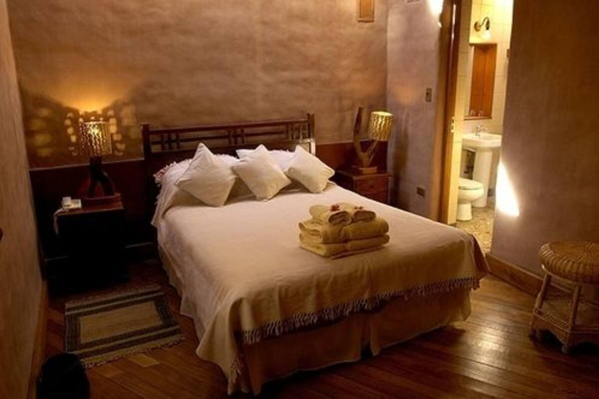 A neatly made bed with white linens and pillows, a bedside lamp, and a small table with a lamp.