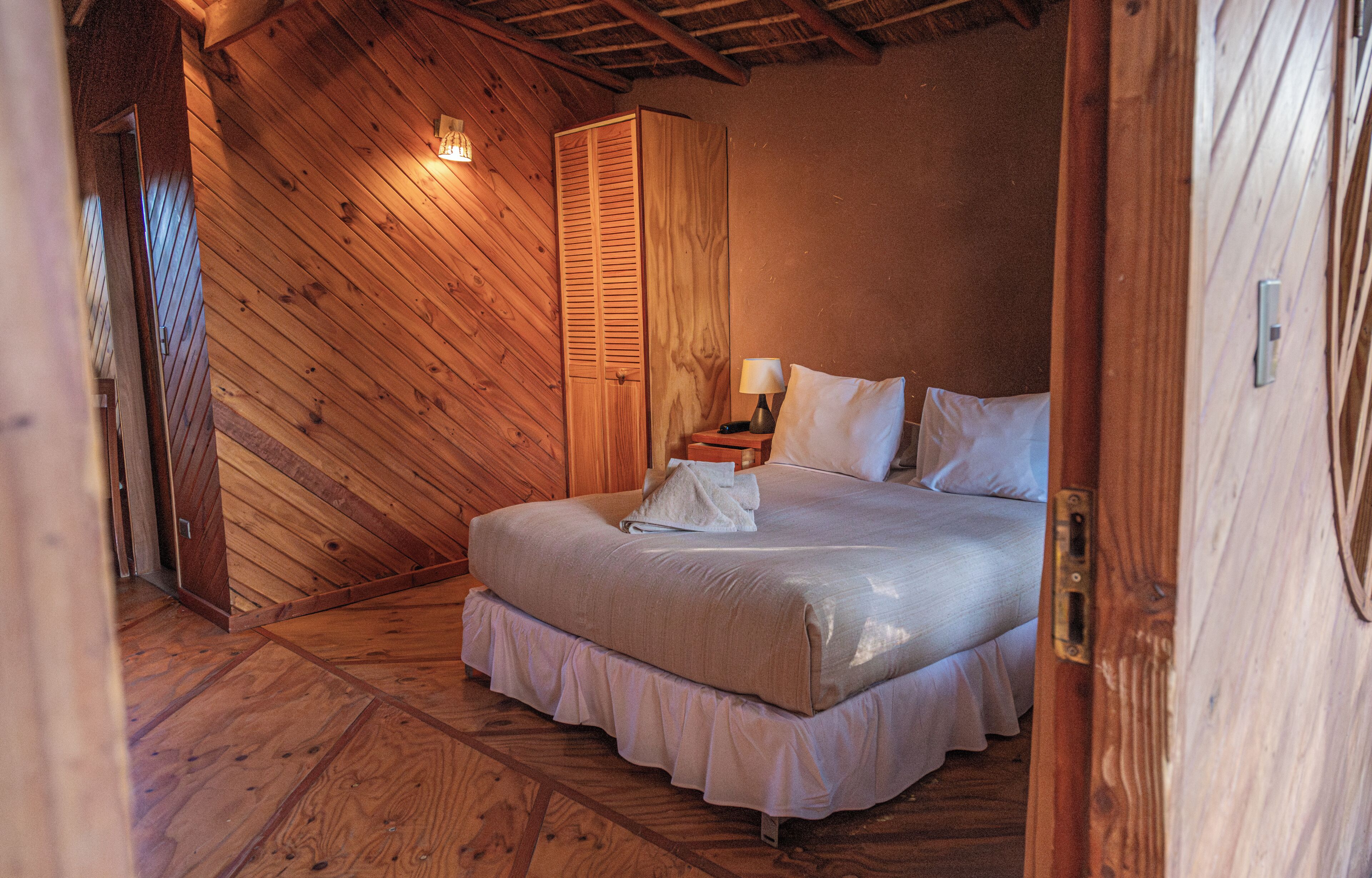 Een kamer met een bed, nachtkastje, lamp en garderobe.