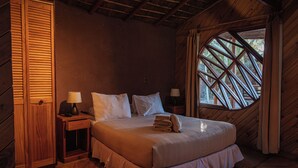 A wooden room with a bed, two nightstands, and a window with a wooden frame. - Hotel Kimal (San Pedro de Atacama)