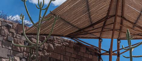 A building with a brick exterior, a wooden structure with a thatched roof, and cacti in the foreground.