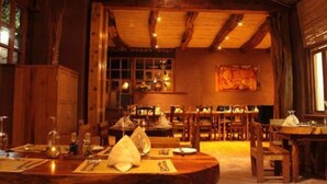 A rustic wooden interior with multiple dining tables and chairs, wooden beams on the ceiling, and a large window on the left. - Hotel Kimal (San Pedro de Atacama)