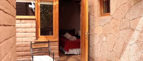 Un edificio de piedra con puerta de madera que da a un dormitorio con cama y una manta roja.