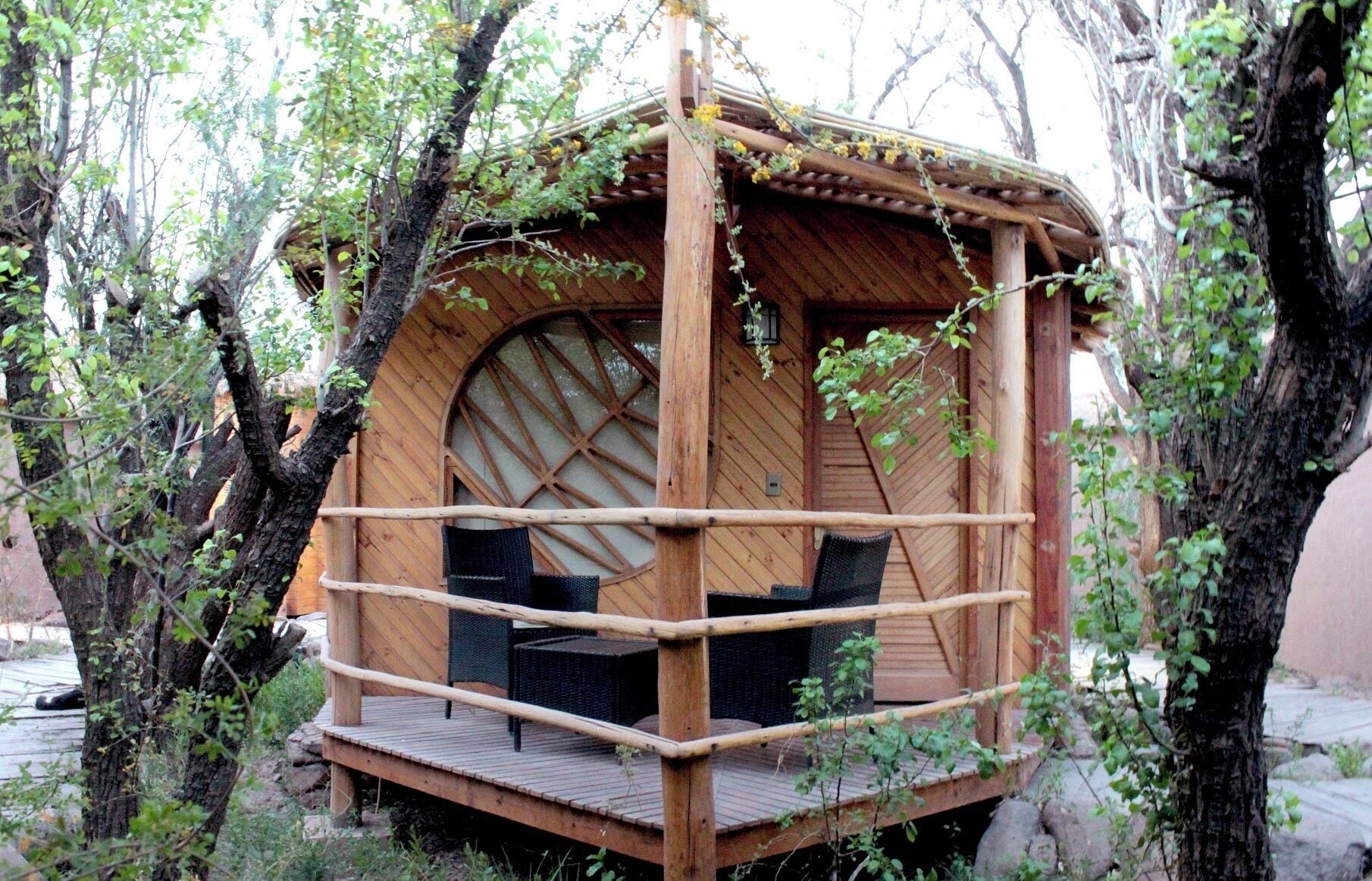 Une cabane en bois perchée dans un arbre, dotée d’une fenêtre circulaire et d’une terrasse en bois.