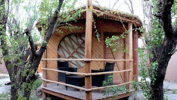 Une cabane en bois perchée dans un arbre, dotée d’une fenêtre circulaire et d’une terrasse en bois.