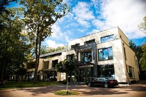 Un hotel moderno con ingresso evidente, un'auto parcheggiata davanti e un'area esterna curata con alberi.