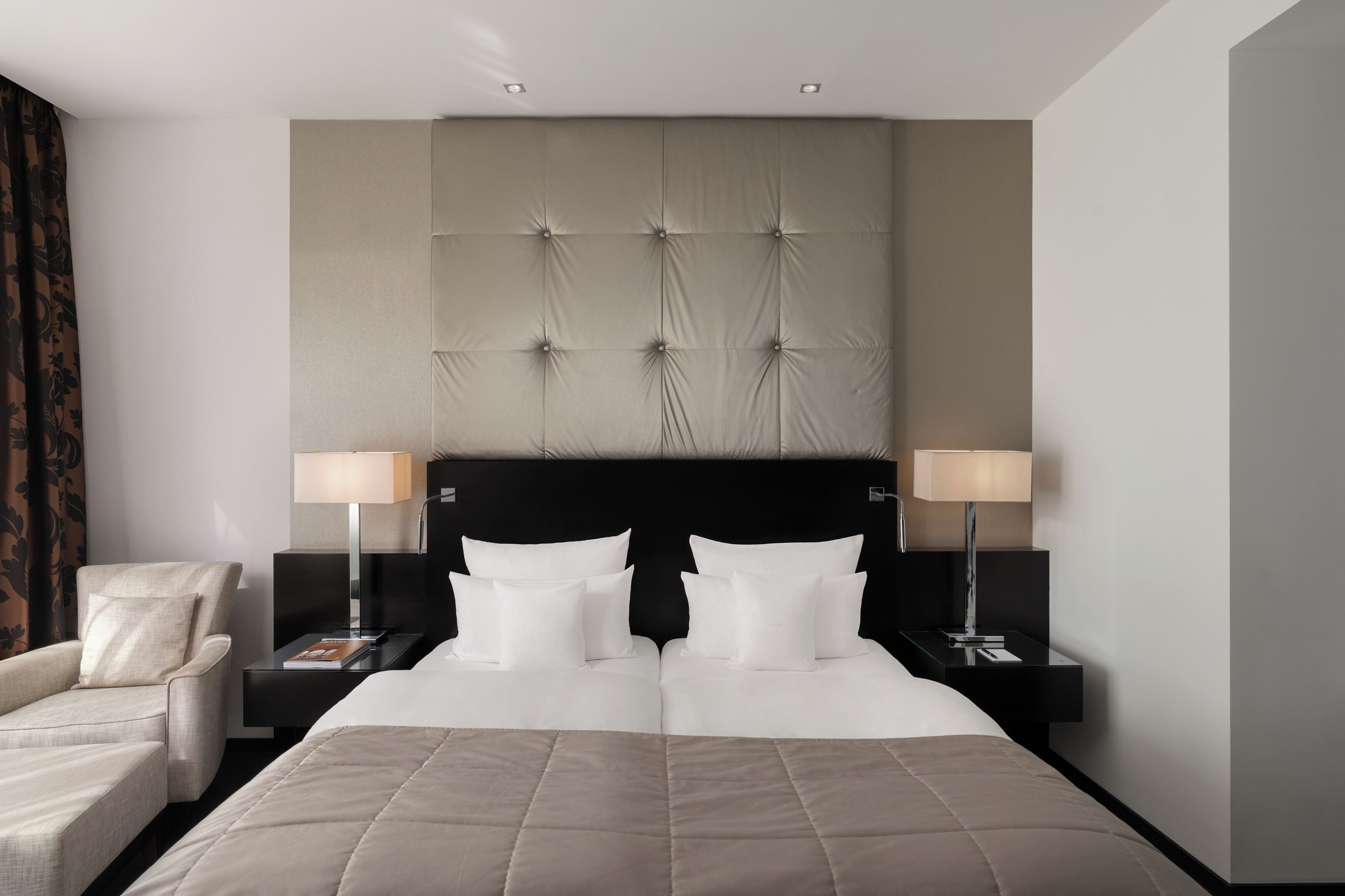A hotel room with a large bed, two bedside tables with lamps, a chair, and a headboard with a tufted design.