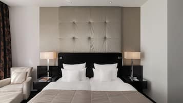 A hotel room with a large bed, two bedside tables with lamps, a chair, and a headboard with a tufted design.