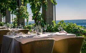 Tavola imbandita con vista sul mare, circondata da sedie in vimini.