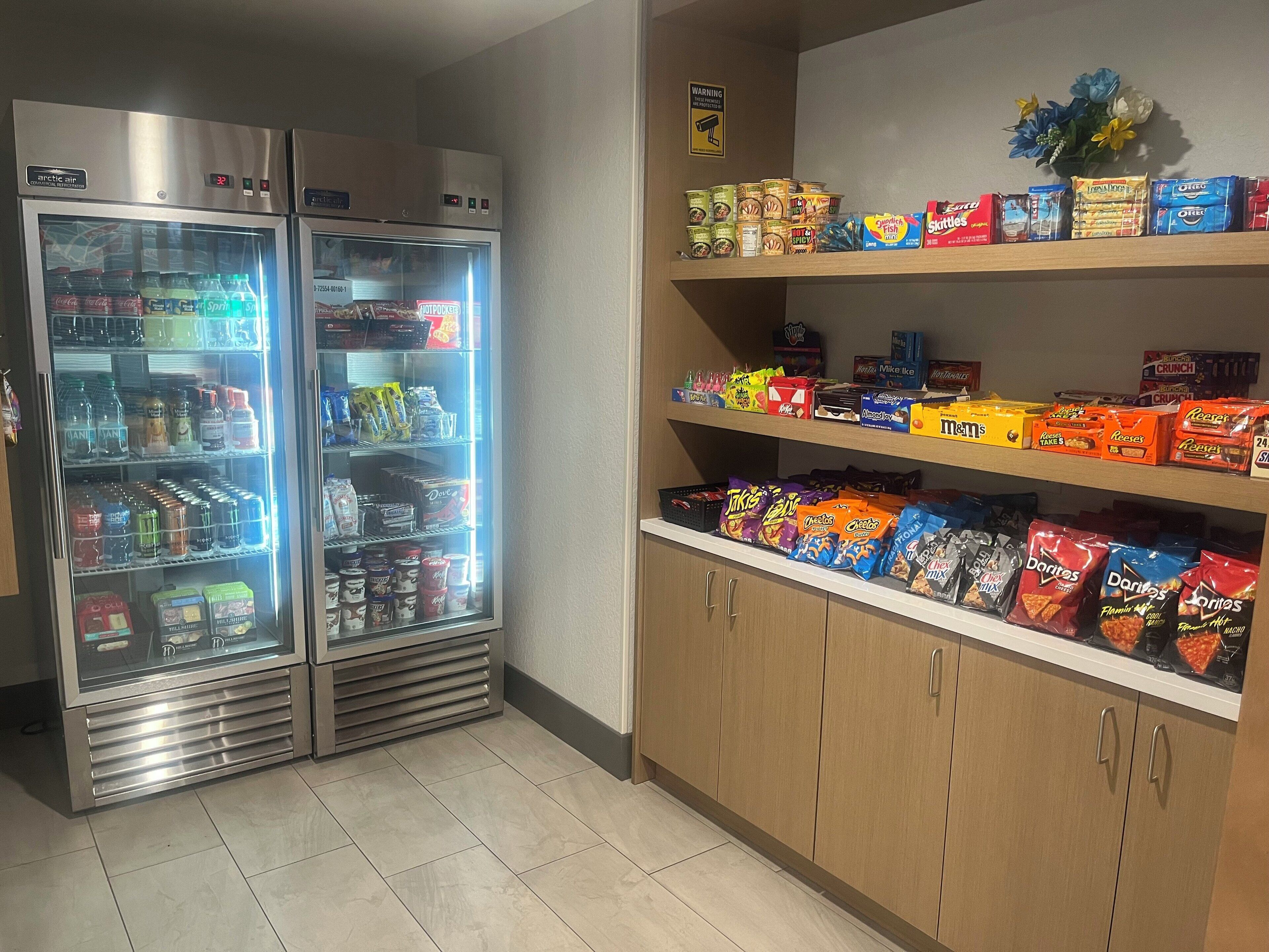A vending machine stocked with beverages and snacks, and a shelf with various packaged food items.