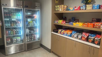 A vending machine stocked with beverages and snacks, and a shelf with various packaged food items.
