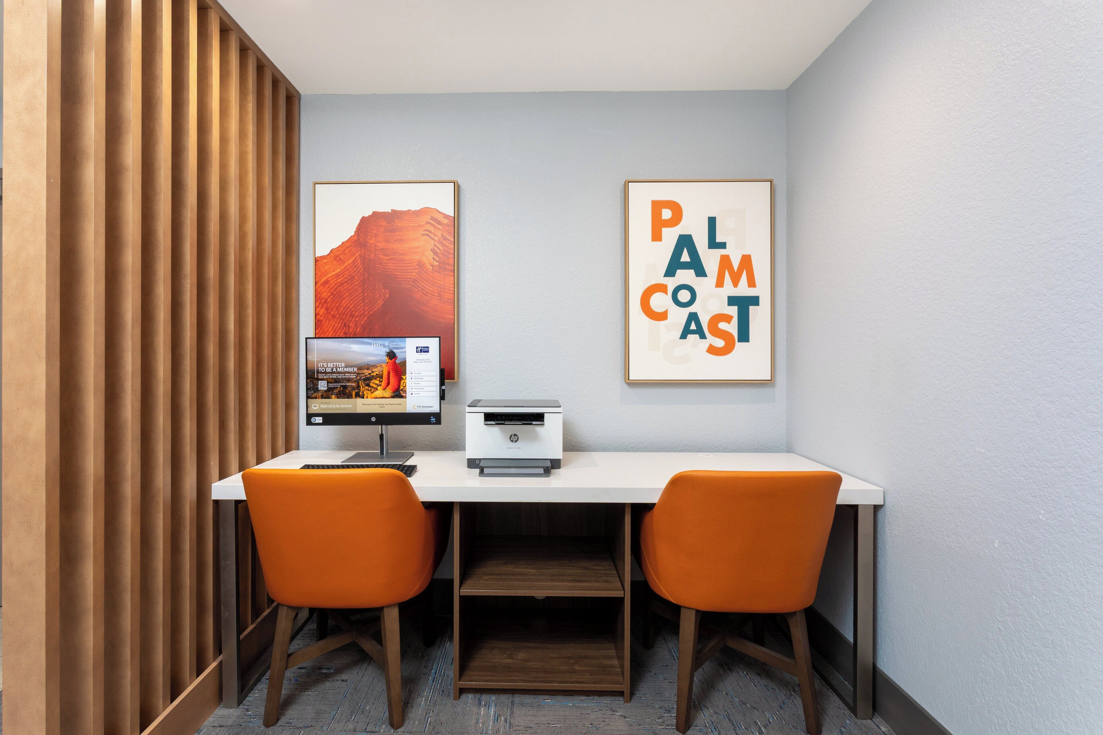 A room with a white desk, two orange chairs, a printer, and two framed pictures on the wall.
