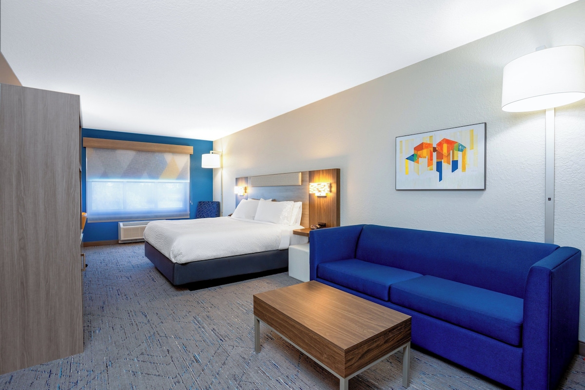 A hotel room with a bed, a blue sofa, a wooden coffee table, and a wall-mounted lamp.