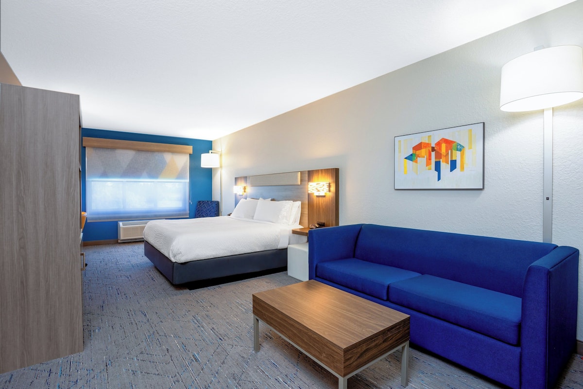 A hotel room with a bed, a blue sofa, a wooden coffee table, and a wall-mounted lamp.