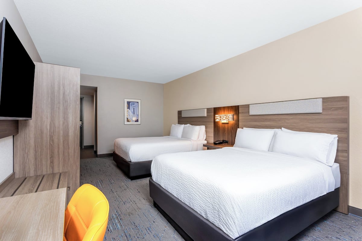A hotel room with two beds, a TV, a desk, and a chair.