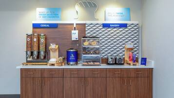 A breakfast station with cereal and bakery options, including Quaker Oatmeal and a grab-and-go sign.