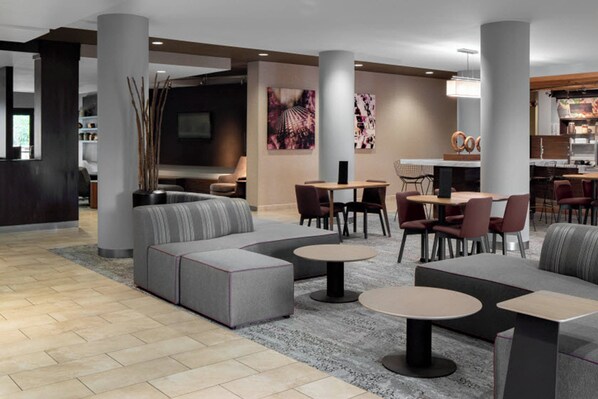 A modern hotel lobby with a sectional sofa, round tables, and a dining area. - Courtyard by Marriott Raleigh North (Raleigh)