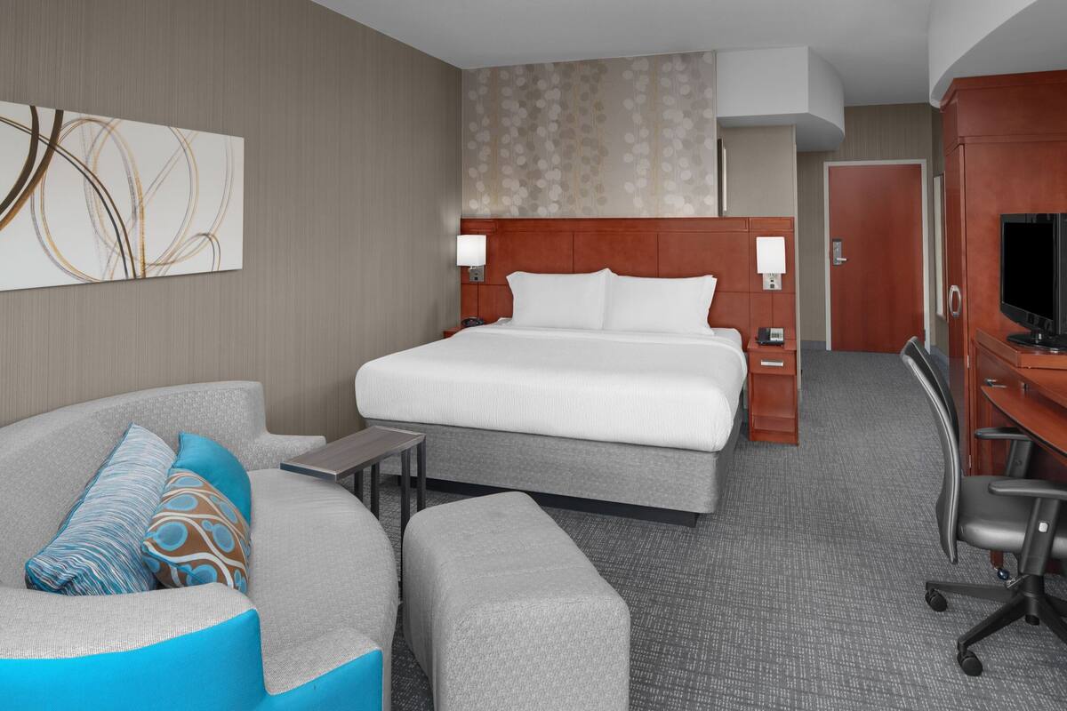 A hotel room with a large bed, a sofa, a desk, and a television.