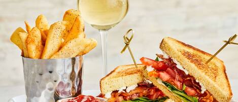 A plate with a grilled sandwich, a glass of white wine, and a container of seasoned fries.