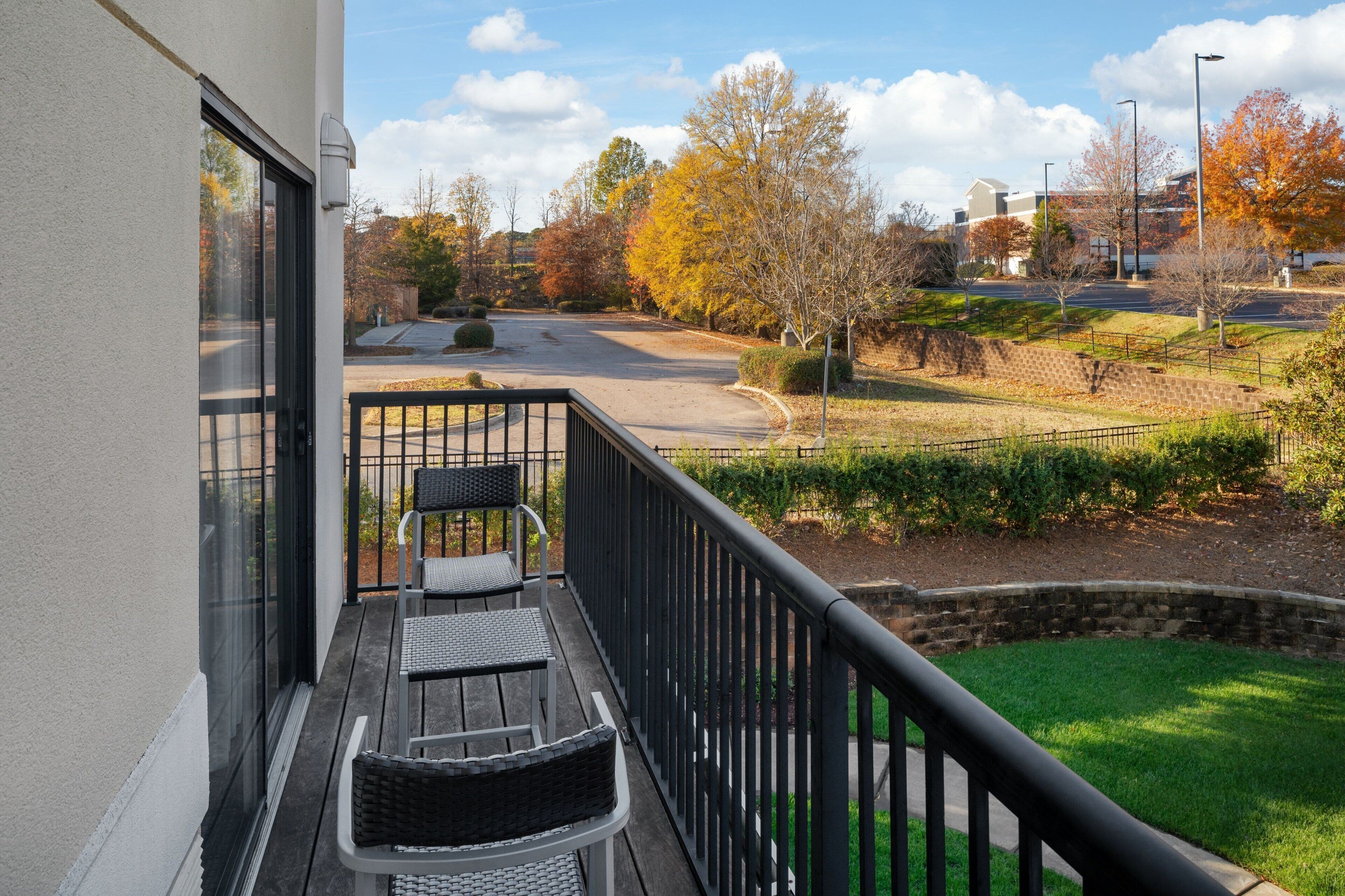 A balcony with a view of a landscaped area, a paved road, and buildings in the distance.