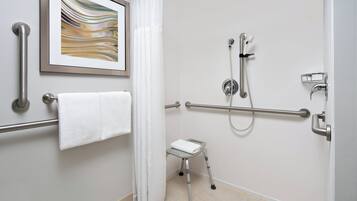 A bathroom with a shower, grab bars, a small stool, and a towel rack.