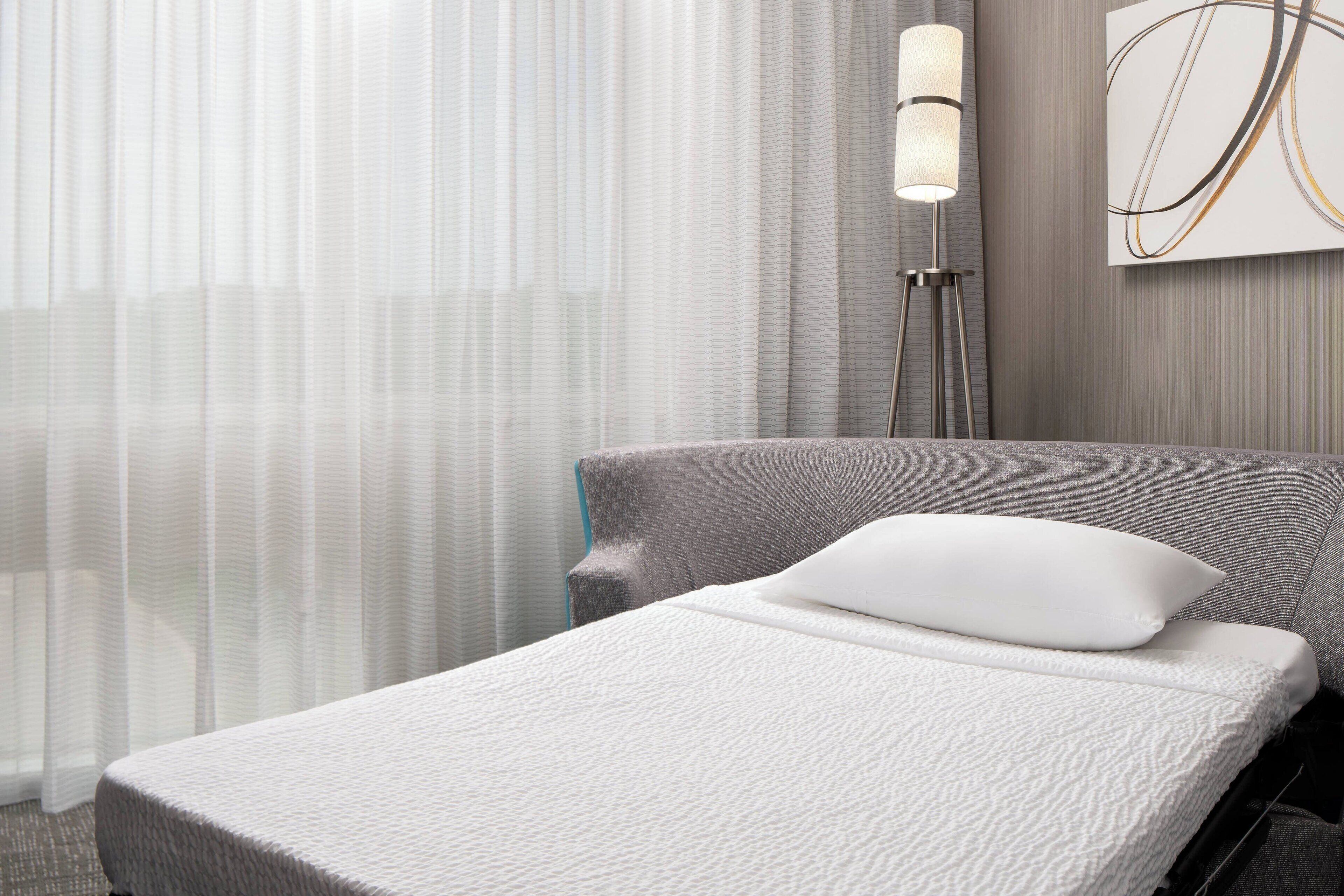 Una cama bien hecha con una almohada blanca y un cabecero gris en una habitación de hotel.