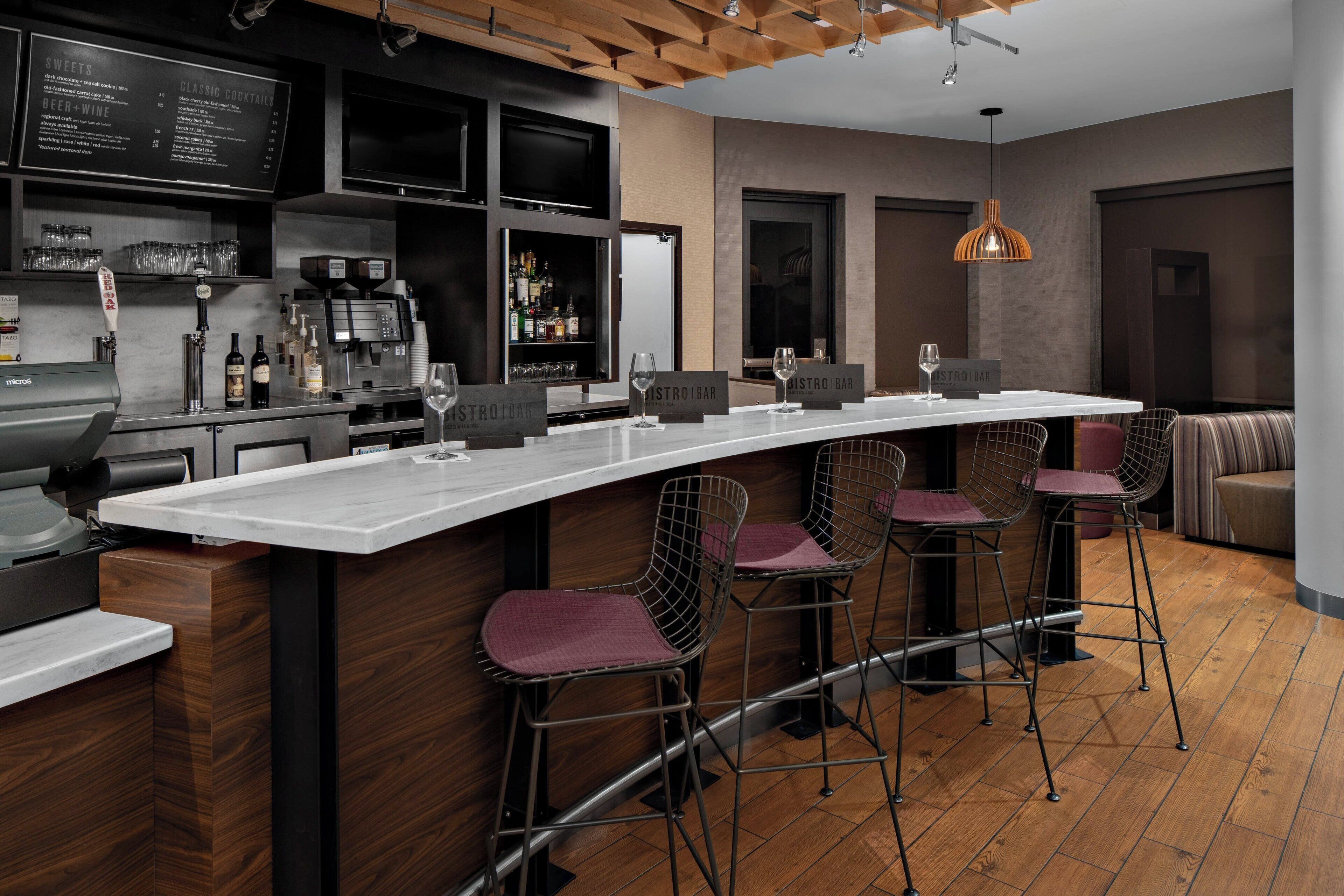 A modern bar area with a long counter, bar stools, and a menu board.
