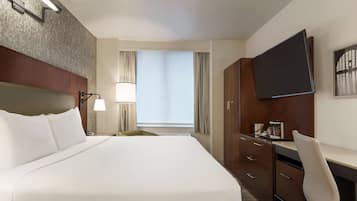 Quarto de hotel com uma cama grande, uma escrivaninha com cadeira, televisão e janela com cortinas.