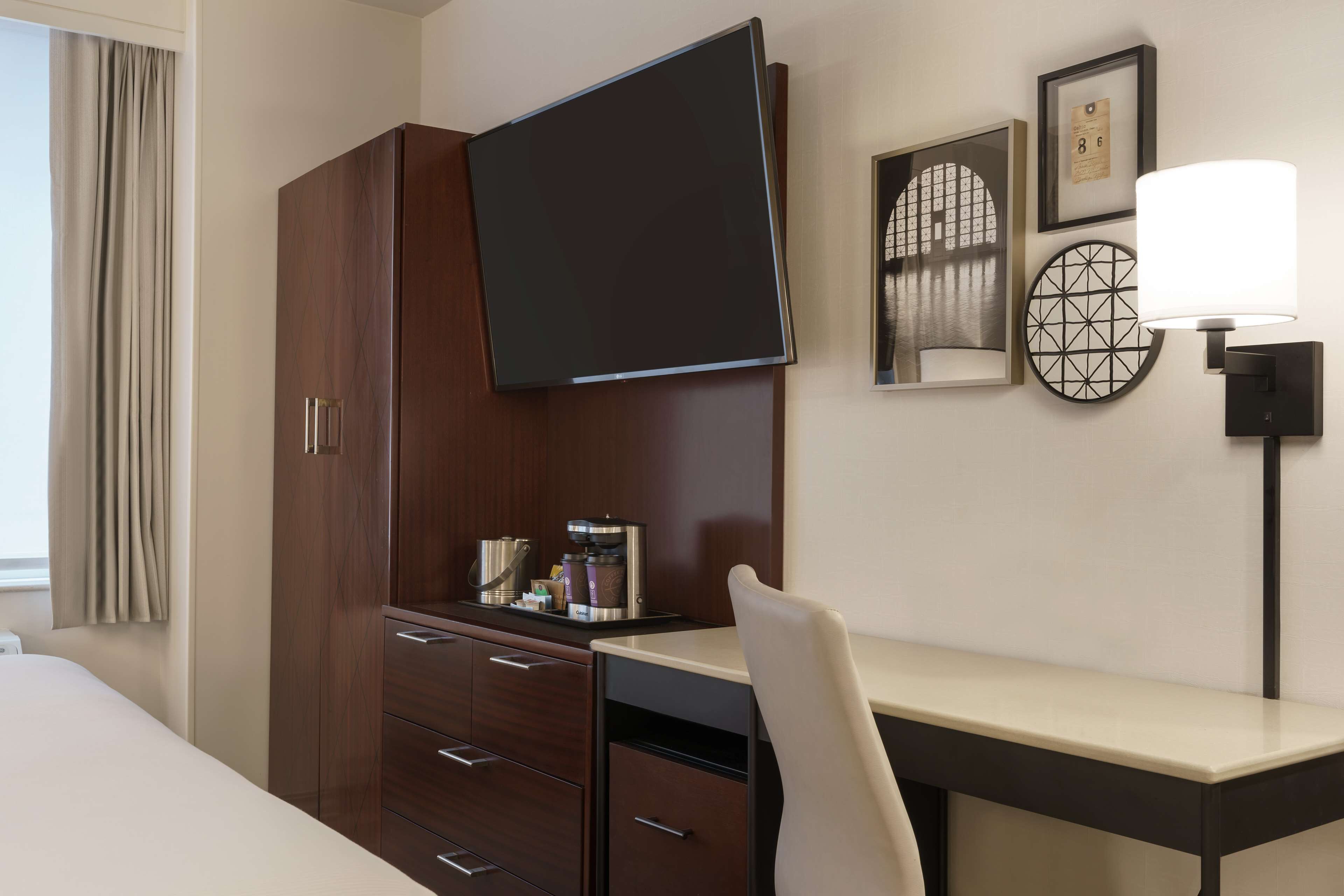 Una habitación de hotel con una cama, un escritorio, una silla, un televisor, una cafetera y una lámpara.