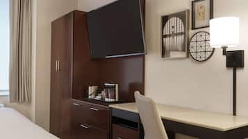 Una habitación de hotel con una cama, un escritorio, una silla, un televisor, una cafetera y una lámpara.